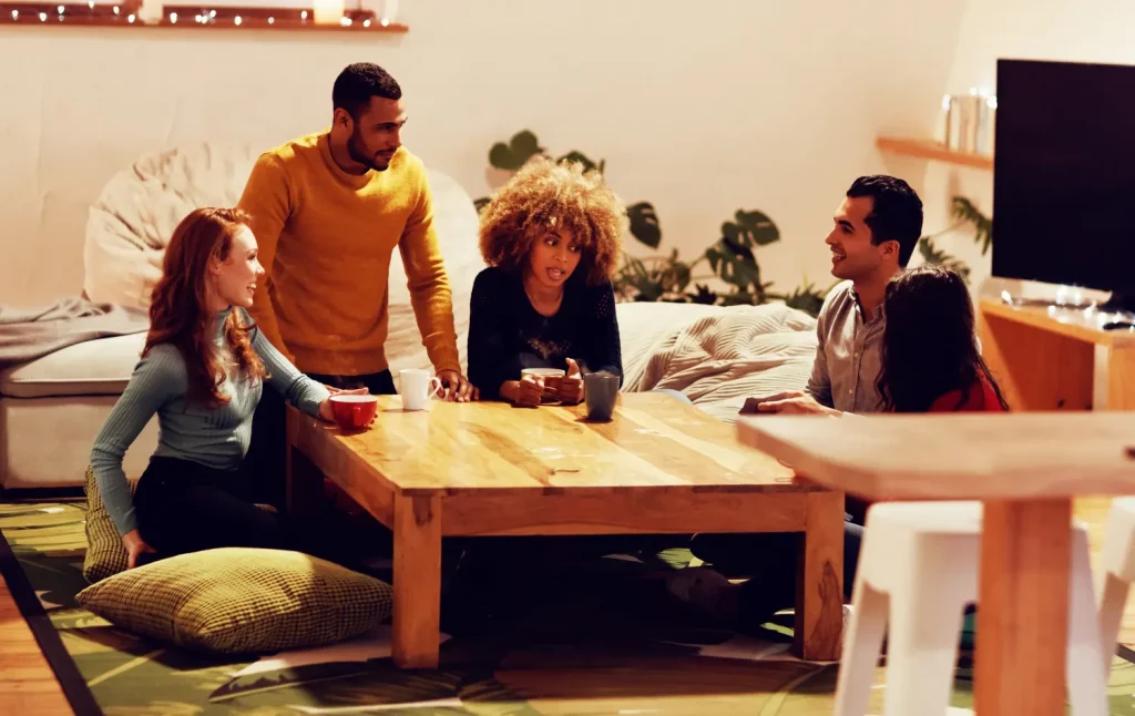 Group of colleagues gathered around a wooden table, discussing about their assessments in a cozy living room setting.